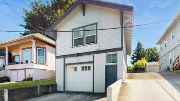 A two-story residential building with a garage, a front porch, and a small front yard.