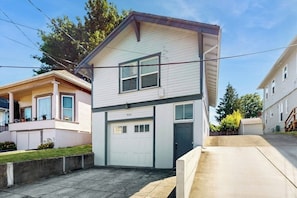 A two-story residential building with a garage, a front porch, and a small front yard.