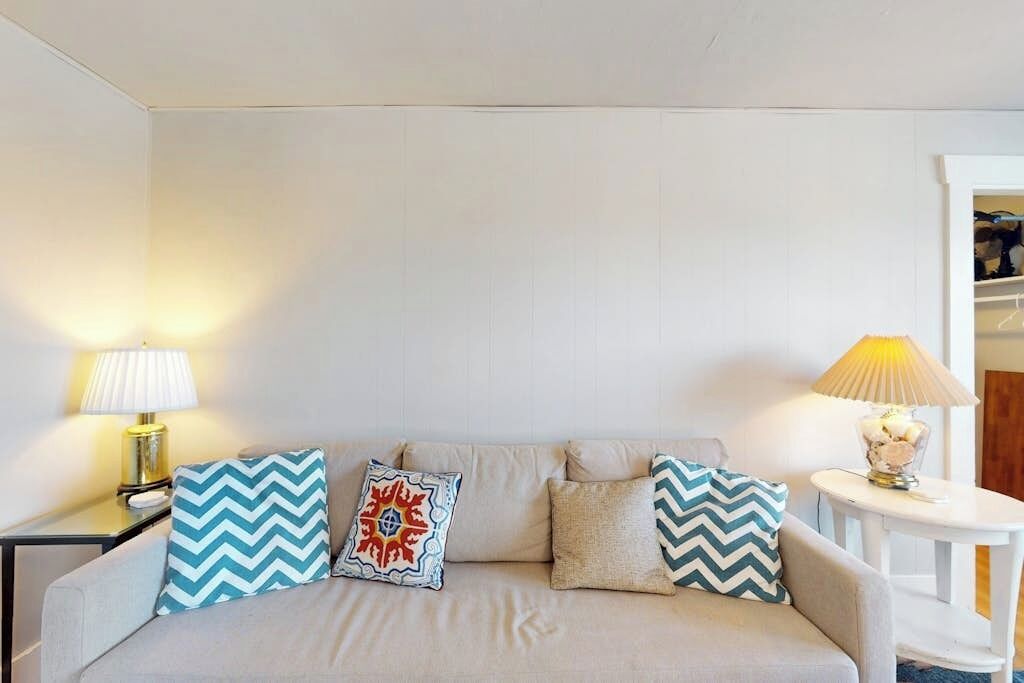 A neutral-colored sofa with patterned cushions, two bedside lamps, and a small table with a lamp.
