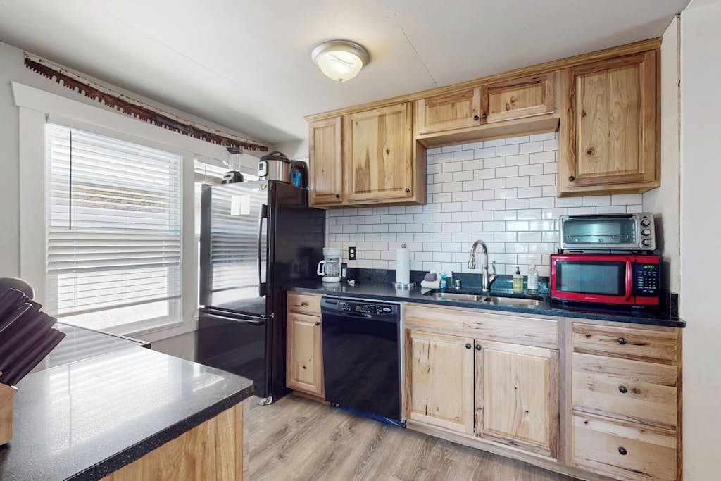 A kitchen with wooden cabinets, a black refrigerator, a dishwasher, a microwave, and a toaster.