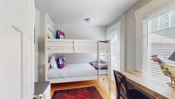 A bunk bed with pillows, a desk with a chair, a rooster decoration, and a window with blinds.