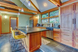 Una cocina con una isla central, taburetes de bar, armarios de madera y vistas a través del ventanal.