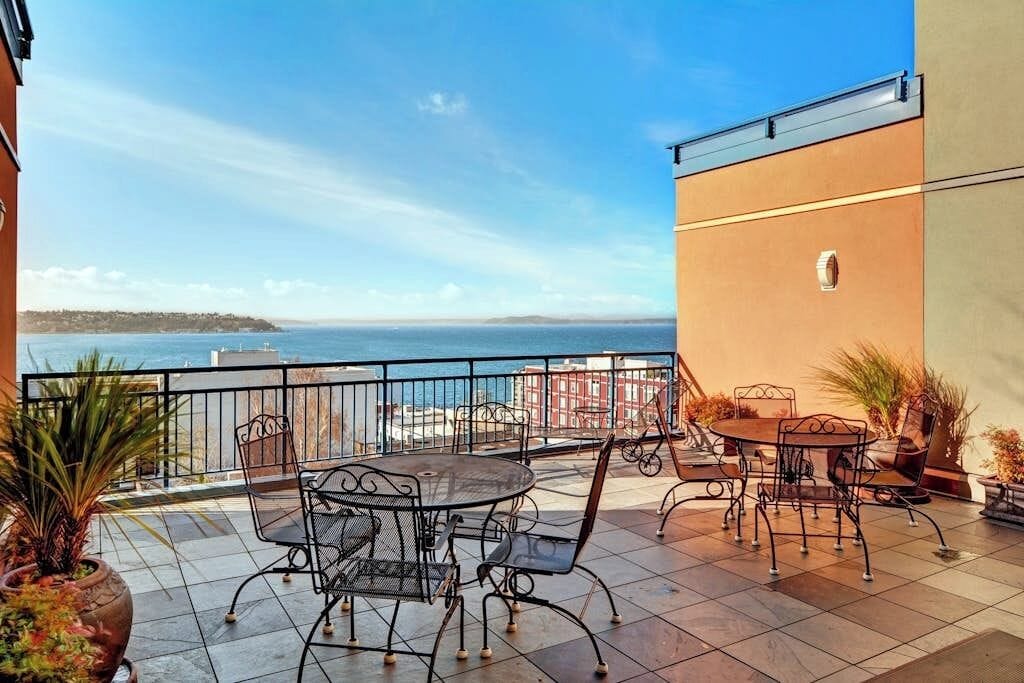 Eine Terrasse mit Gartenmöbeln, Blick auf das Meer und ein Gebäude mit Flachdach.