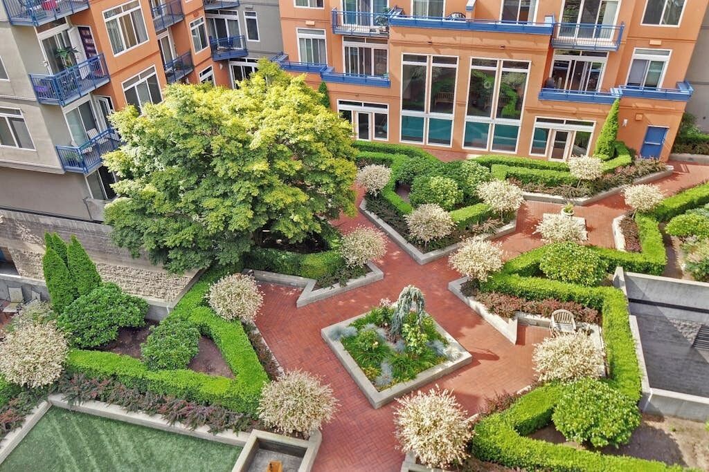 A multi-story residential building with balconies, a central courtyard with manicured gardens, and a large tree.