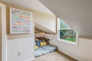 Eine gemütliche Leseecke mit einem Wandbild aus Wortwolken, einer gepolsterten Bank und Lichterketten.