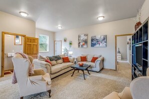A living room with a sofa, armchair, and coffee table, a television, and artwork on the walls. - Idyllic woodsy 6BR with firepit & two kitchens (Camano Island)