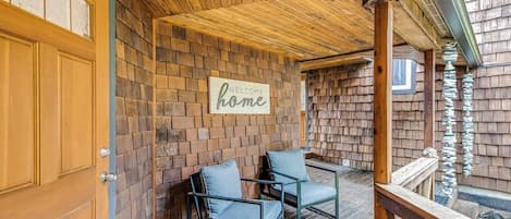 Une terrasse en bois avec deux chaises, une porte en bois et une pancarte « Bienvenue chez vous » accrochée à un mur de briques.