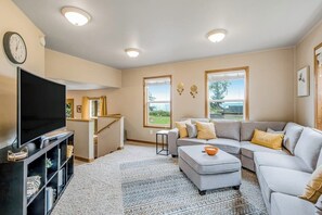 Ein Wohnzimmer mit Flachbildfernseher, grauem Sofa, Couchtisch und großem Fenster mit Aussicht.