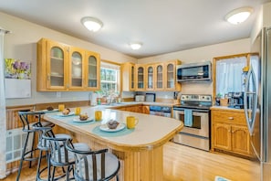 A kitchen with wooden cabinets, a central island with bar stools, a microwave, and a refrigerator. - Idyllic woodsy 6BR with firepit & two kitchens (Camano Island)