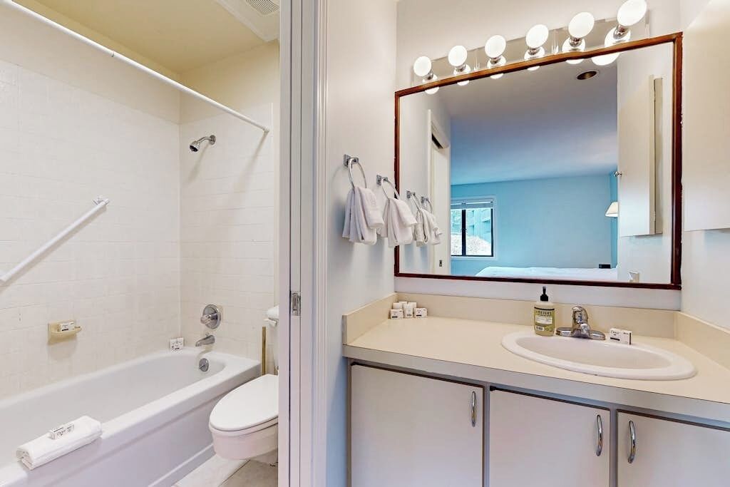 A bathroom with a bathtub, toilet, and a vanity with a mirror and lights.