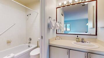 A bathroom with a bathtub, toilet, and a vanity with a mirror and lights.