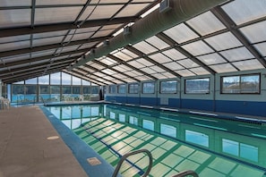 An indoor swimming pool with a glass ceiling, clear pool water, and a view of the outdoors.