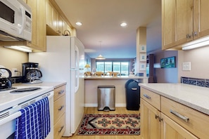 A compact kitchen with wooden cabinets, a white refrigerator, a stove, and a trash bin.