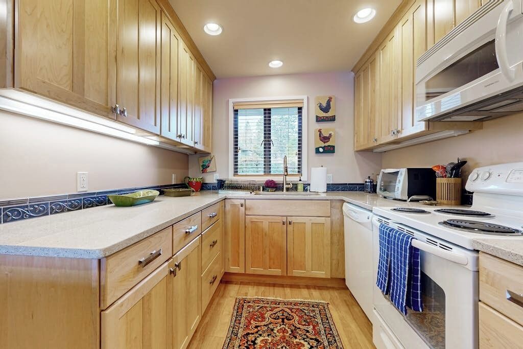 Una cocina con gabinetes de madera, microondas, horno y ventana con persianas.