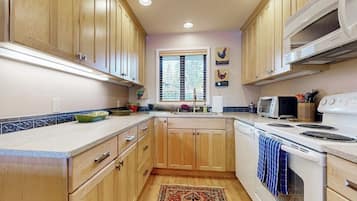 Una cocina con gabinetes de madera, microondas, horno y ventana con persianas.