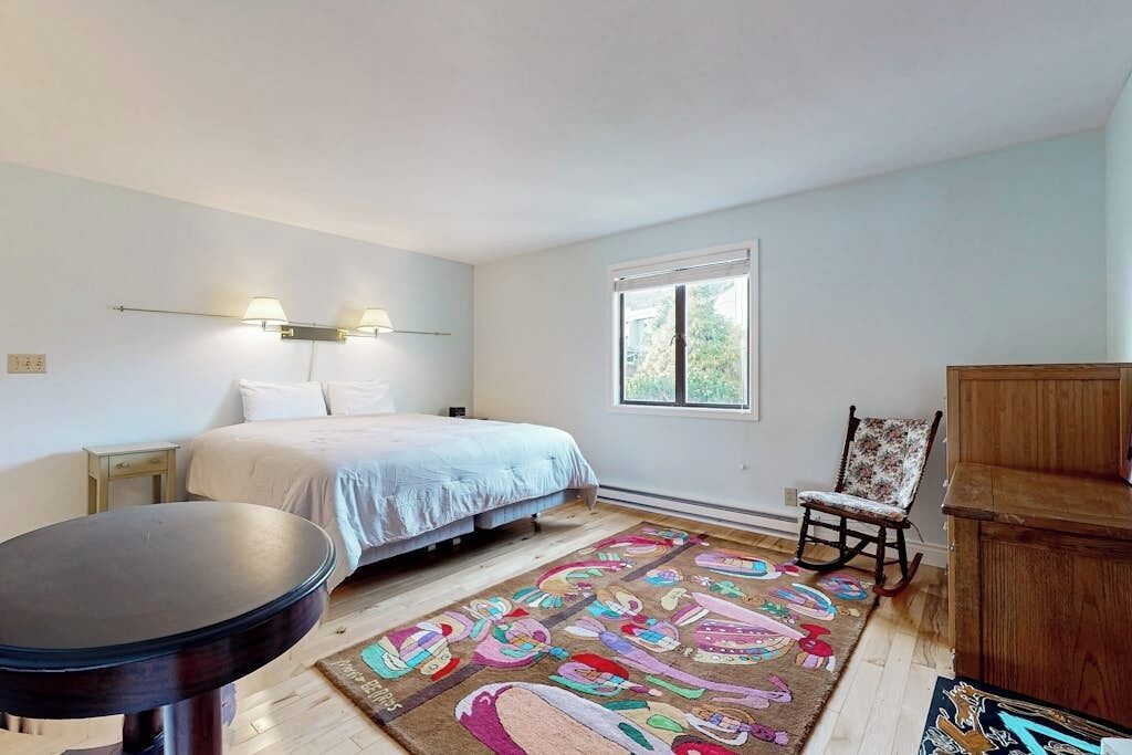 A bedroom with a bed, a chair, a table, and a window.
