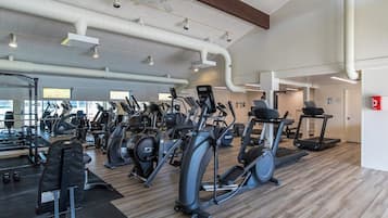 A gym with various cardio machines, weightlifting equipment, and a mirror wall.