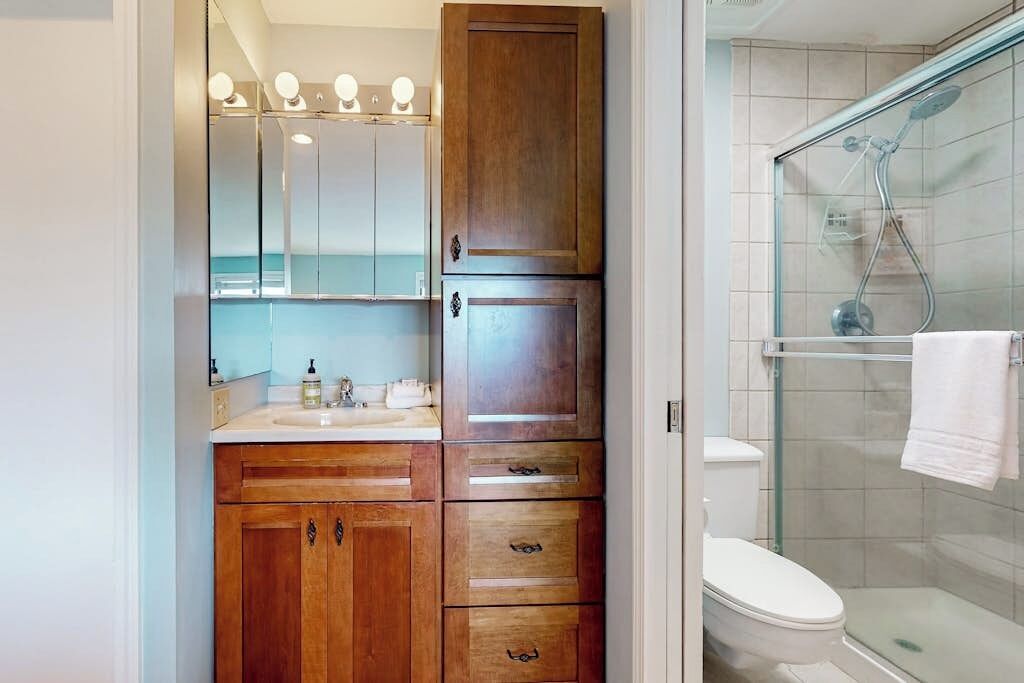 A bathroom with a wooden vanity, a mirror, a toilet, and a glass shower enclosure.