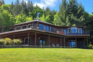 A two-story wooden cabin with a balcony, surrounded by a well-maintained lawn and dense forest. - 2BR idyllic retreat with a hot & grill - dogs ok (Port Angeles)