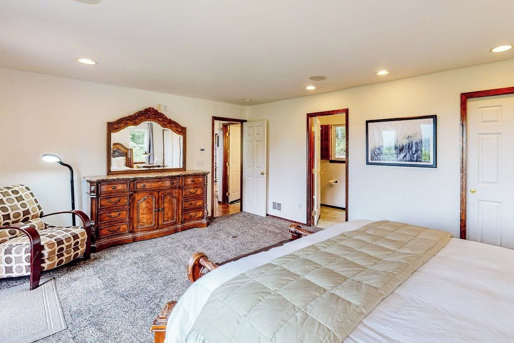 A bedroom with a bed, dresser, chair, and a door leading to another room.