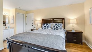 A bedroom with a bed, bedside tables, a nightstand, a mirror, and a door.