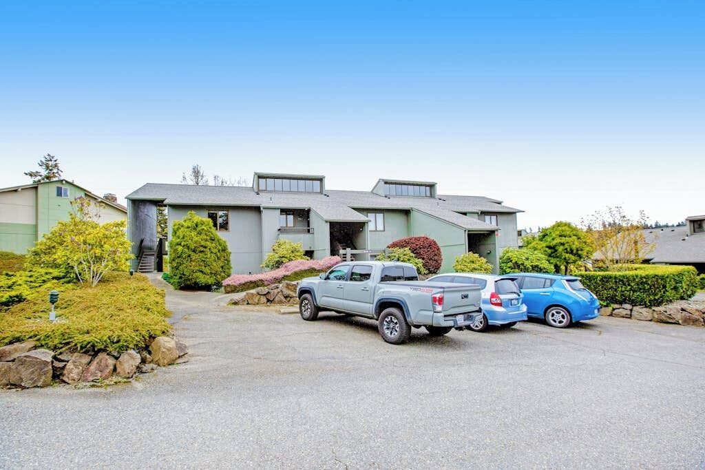 Un edificio residencial con entrada para coches, una camioneta estacionada y un coche azul.