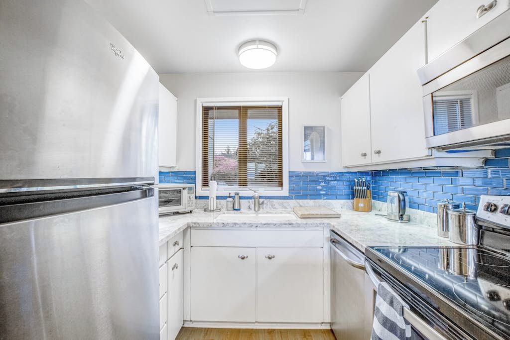 Una cocina moderna con electrodomésticos de acero inoxidable, armarios blancos y salpicadero de azulejos azules.