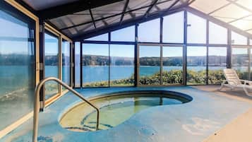 An indoor swimming pool with a view of a lake and hills.