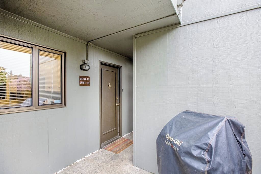 Fachada de un edificio con una puerta que indica 'Bldg. 11 Unit 13', un objeto cubierto y una ventana con persianas.