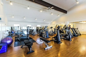 Un gimnasio con equipo de ejercicio variado, incluyendo cintas de correr, bicicletas estáticas y pesas libres.