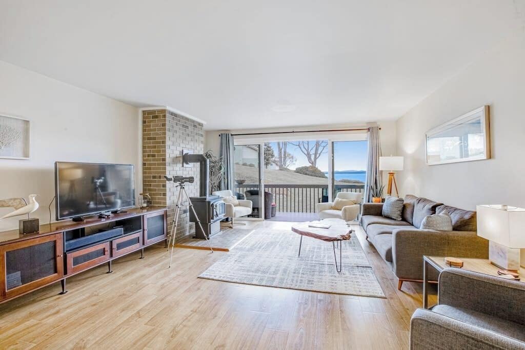 A spacious living room with a large TV, comfortable seating, a fireplace, and a view of the outdoors.