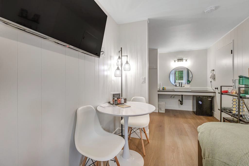Een moderne keuken met witte kasten, een ronde eettafel met stoelen, een inbouwoven en een aan de muur bevestigde televisie.