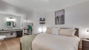 A modern bedroom with a large bed, a bedside table, a mirror, a nightstand, and a wall-mounted shelf with books. - Perfectly Located Studio Mountainview Mount Walker (Quilcene)