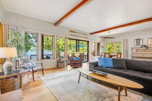 A spacious living room with a large sofa, a coffee table, and a fireplace. There are multiple windows providing natural light and views of the outdoors. - 4BR charming lakeside home with beach access (Olympia)