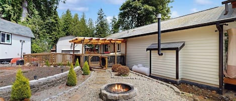 A backyard with a fire pit, wooden deck, and a covered seating area.