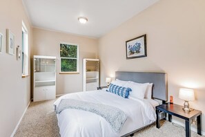 Ein Schlafzimmer mit einem Bett, Nachttischen, einem Fenster und einem gerahmten Bild an der Wand.