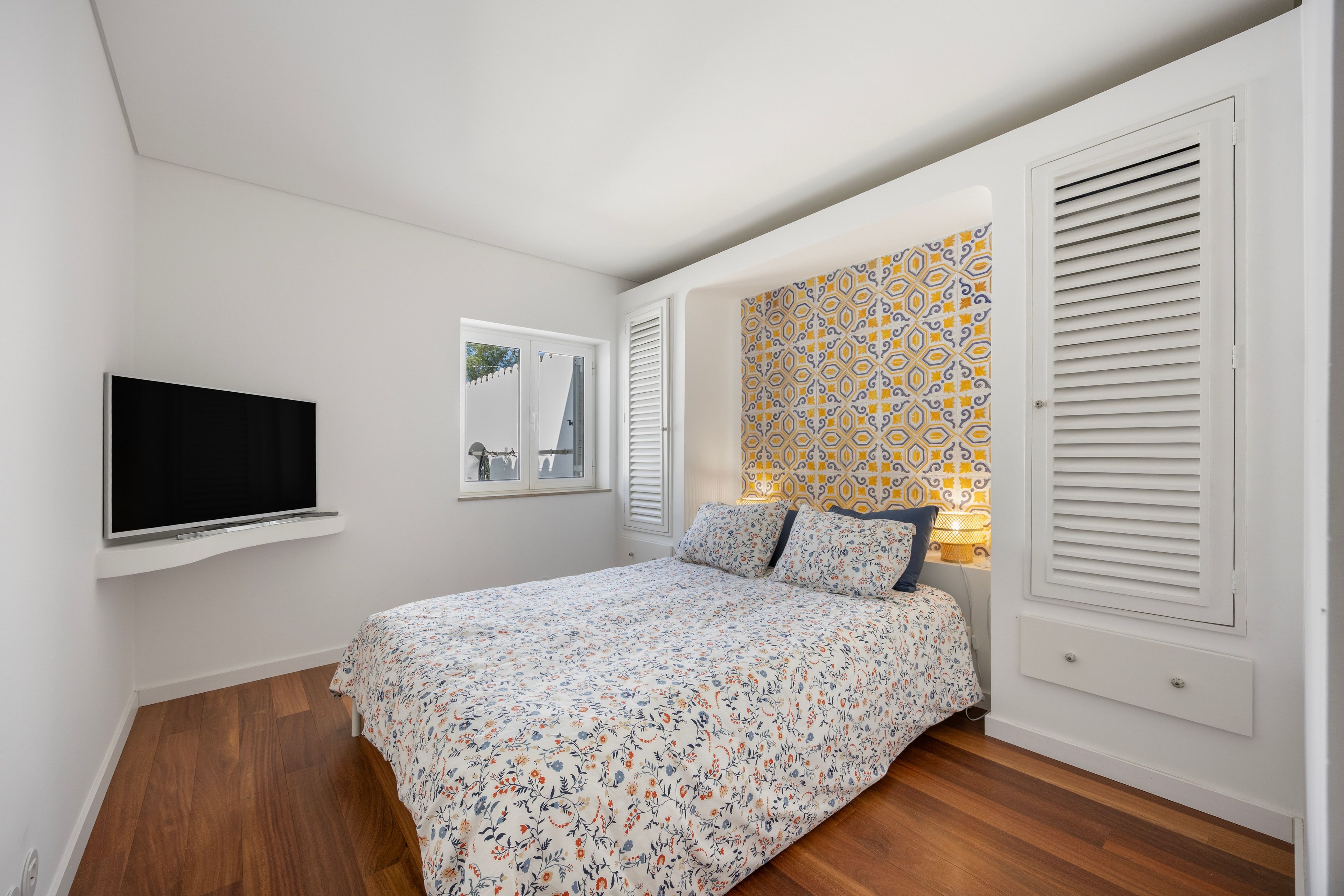 Une chambre à coucher avec un lit, un téléviseur fixé au mur, une fenêtre et un motif décoratif sur le mur.