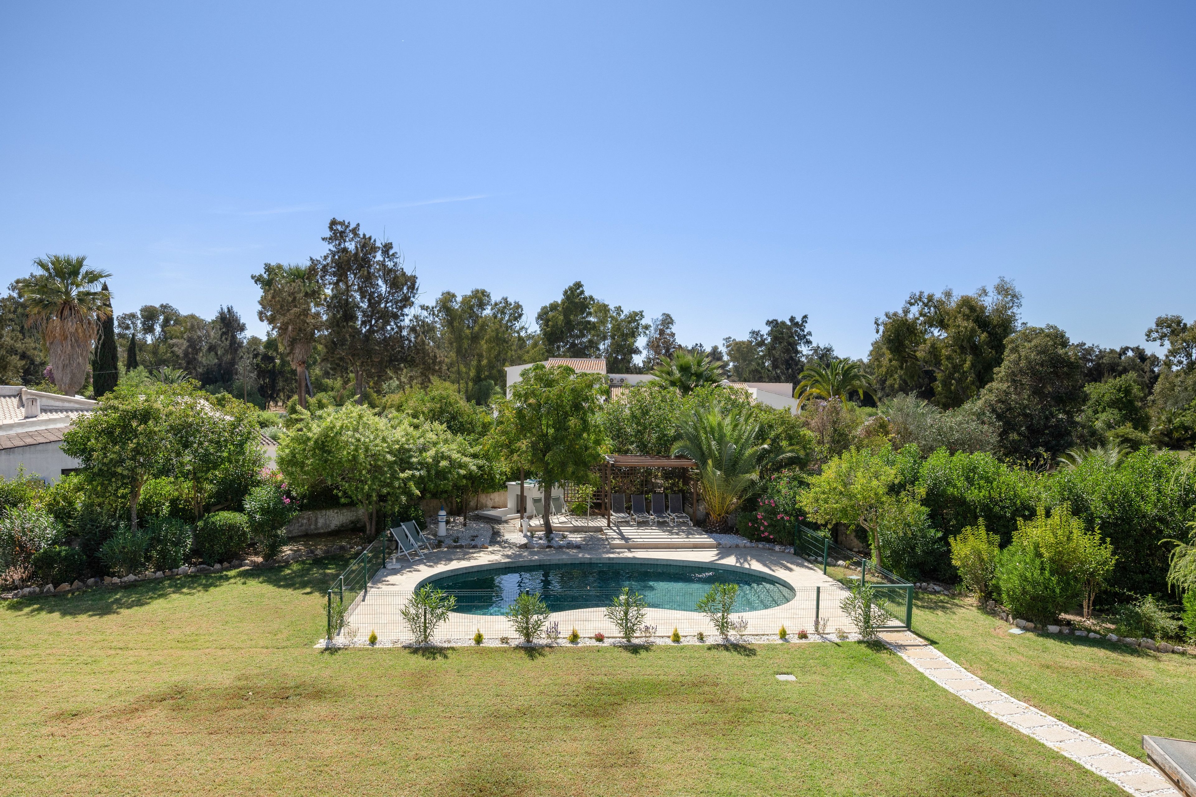 A swimming pool surrounded by a well-maintained lawn and various trees.