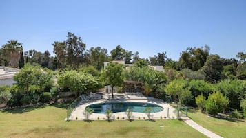 A swimming pool surrounded by a well-maintained lawn and various trees.