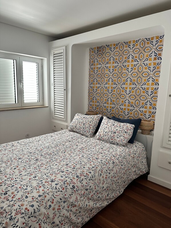 A bedroom with a bed, a window with blinds, and a patterned wall.
