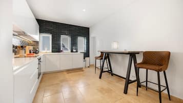 A modern kitchen with white cabinetry, a black tiled backsplash, and a dining area with a table and two stools.