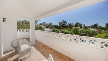 Un balcon doté de meubles en osier et offrant une vue sur la verdure et les bâtiments.