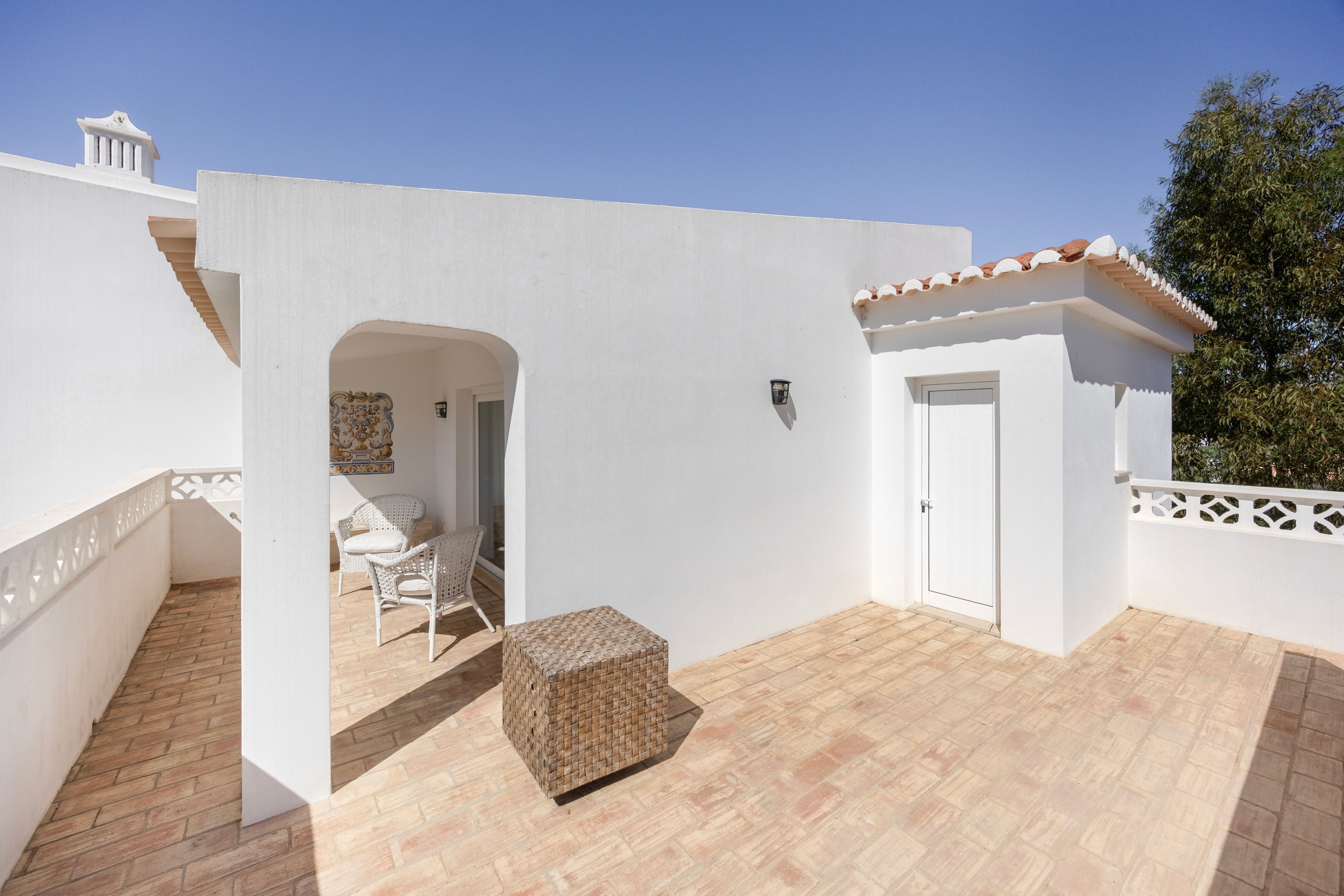 A white building with a tiled roof, a door, and a small balcony with wicker furniture.