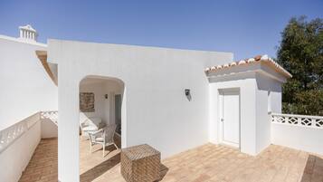 A white building with a tiled roof, a door, and a small balcony with wicker furniture.