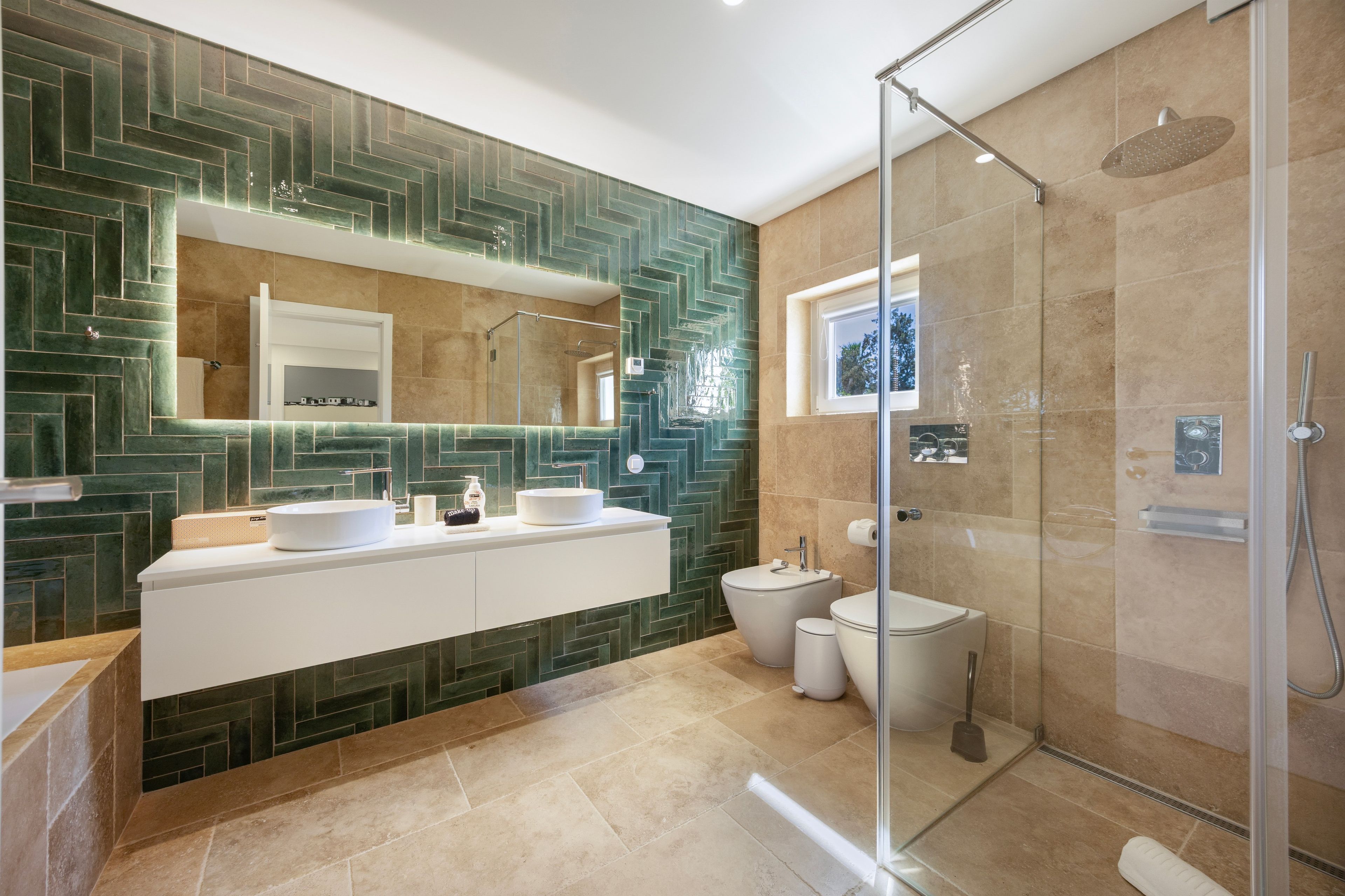Un baño moderno con ducha envuelta en cristal, tocador con doble lavabo y un espejo grande.