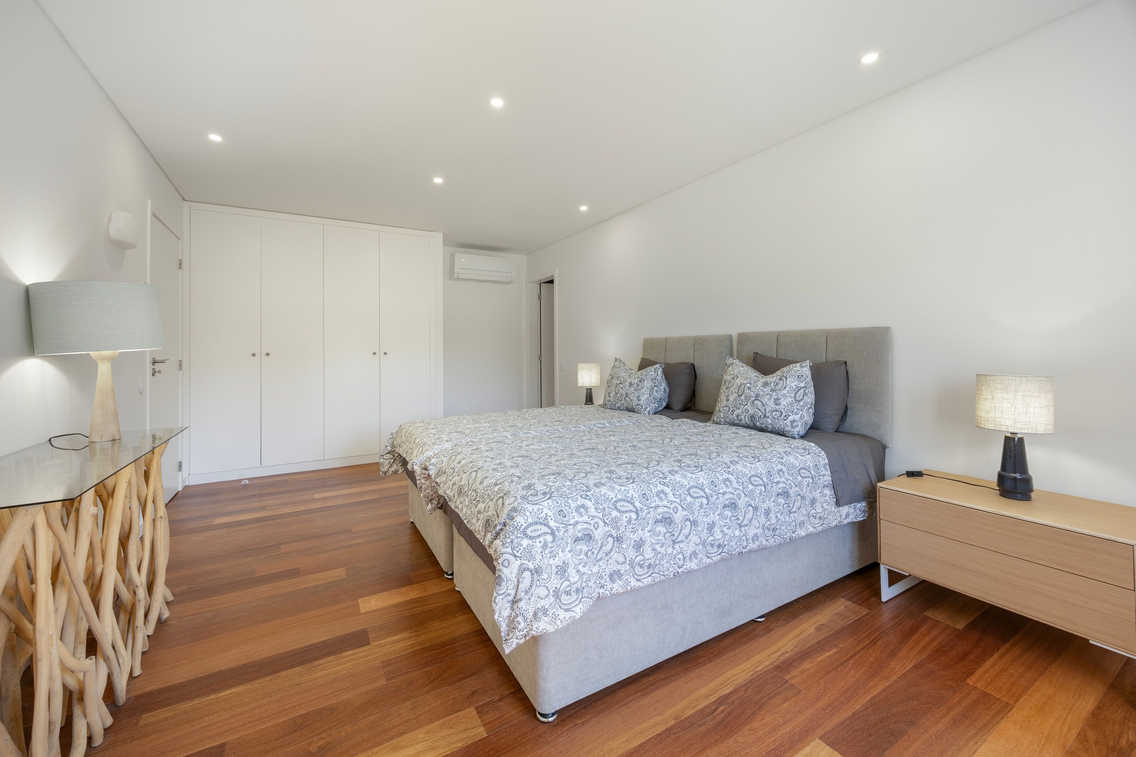 A modern bedroom with a bed, bedside tables, a wardrobe, and a wooden floor.