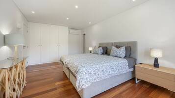A modern bedroom with a bed, bedside tables, a wardrobe, and a wooden floor.