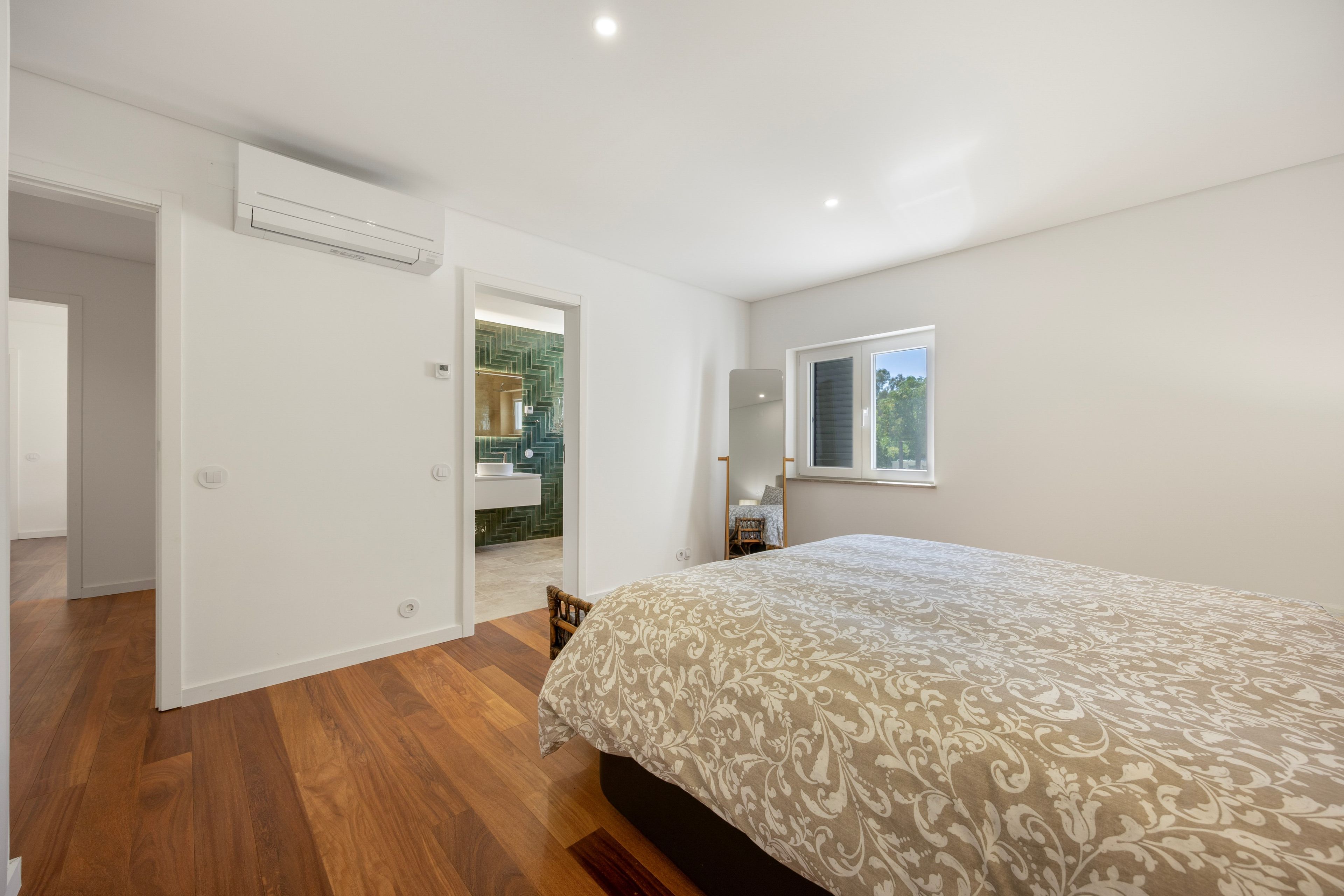Une chambre à coucher avec un lit, une fenêtre et une salle de bain visible à travers une porte ouverte.