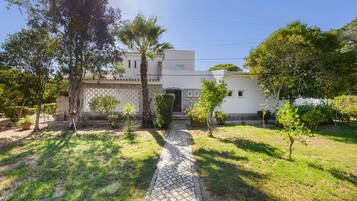 A residential property with a paved driveway leading to a white building with a tiled roof.