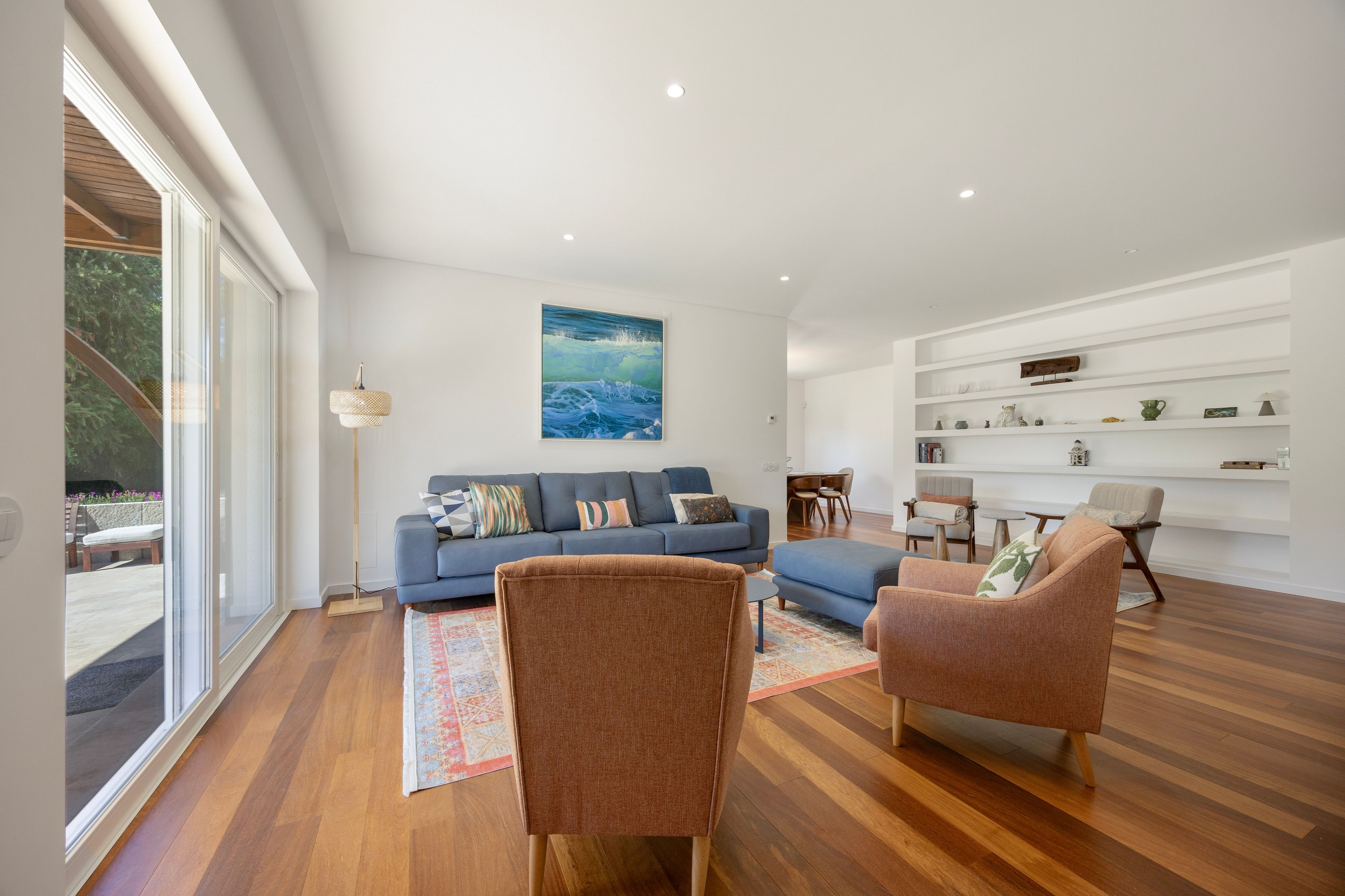 Un salon moderne avec un canapé bleu, deux fauteuils, une lampe sur pied et un tableau accroché au mur.